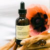 Bottle of Fresh Pickins Farm Holy Basil Extract held by a person with a poppy flower in the background