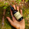 Hand holding a bottle of Fresh Pickins farm Holy Basil Extract on a mossy ground