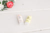 Two Fresh Pickins Farm lip balm tubes on a white surface with flowers in the background