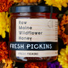 Jar of Fresh Pickins Farm Raw Maine Wildflower Honey with a floral background