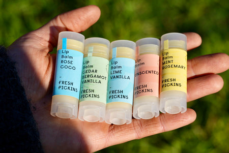 Hand holding 5 lip balm tubes with labels against a blurred green background