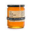 A jar of Fresh Pickins Farm  Raw Maine Wildflower Honey. The honey is visible through the clear glass jar and has a yellow color.