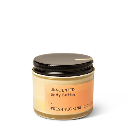 A jar of unscented body butter with a black lid and a label that reads 'UNSCENTED Body Butter FRESH PICKINS'.